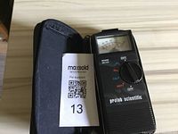 Prolab Scientific analog sound meter positioned beside a zippered case and a MaxSold auction tag number 13 visible in the case pocket.