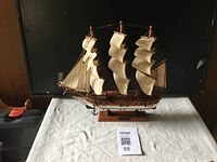 Front angled view of the wooden model tall ship Gorchfock with three masts and cream-colored sails on a white tablecloth.