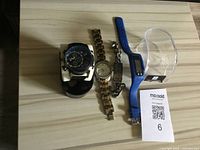 Wide shot showing five wristwatches including analog and digital styles on a light wood surface, along with a Marsold label.