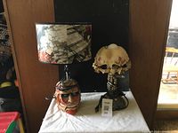 Overall view of the two lamps on a table showing bases and shades including the Attack on Titan face lamp and the skull lamp.
