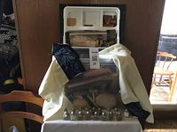Photo showing a plastic bin filled with various wooden craft pieces. In front of the bin are eight small glass salt and pepper shakers with silver lids. Beige and dark patterned cloths are draped around the bin.