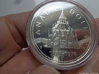 Close-up of the 1976 Canadian silver dollar coin in a clear protective round case showing detailed engraving and inscriptions.