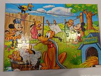 Completed colorful Disney backyard scene puzzle featuring Mickey Mouse, Minnie Mouse, Pluto and other animal characters with laundry line and fence background.