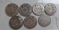 Photo of seven Canadian 50 cent coins from the 1940s, showing the reverse with the coat of arms.