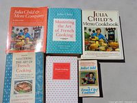 Six Julia Child French cooking cookbooks arranged on a table showing front covers including Mastering the Art of French Cooking volumes, Julia Child & More Company, Julia Child's Menu Cookbook, and The French Chef Cookbook.