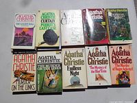 Top view of 10 Agatha Christie paperback books, titles visible include The Golden Ball, Curtain: Poirot's Last Case, The Murder on the Links and more.