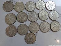 Sixteen coins laid out in rows on white surface showing reverses with Coat of Arms.