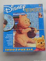 Photo of the puzzle box showing the Disney Photomosaics Winnie the Pooh 1000-piece puzzle with a close-up circle showing mosaic detail.