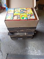 Stack of four cardboard boxes filled with vintage paperback books, covers visible on top layer showing colorful romantic illustrations.