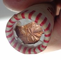 Close-up image showing the end penny with the 1980 date and maple leaf design through the opened end of a red and white striped coin roll.