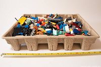 Top-down view of a small tray containing many loose LEGO pieces of various sizes and colors, with a measuring tape showing about 12 inches across.