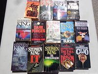 Photo showing 15 Stephen King paperback books arranged on a white surface, covers visible.