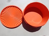 Photo shows an orange round Tupperware storage container and its matching lid with radial textured pattern, placed on a flat surface.