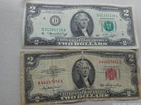 Two United States $2 bills, one in good condition with green seal, the other heavily used with red seal.