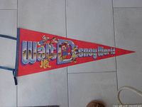 Full view of the red felt pennant with Walt Disney World logo and Disney characters Mickey Mouse, Donald Duck, Goofy, and Pluto