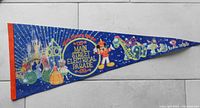 Photo of a vintage Disney Main Street Electrical Parade triangular pennant with colorful parade graphics and an orange trim on a tiled floor.