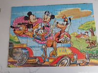 Fully assembled puzzle showing Mickey Mouse, Minnie, Pluto, Donald, and Goofy in a red and yellow vintage car driving scene outdoors with bright blue skies and green landscape