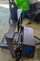 Side angled view of black metal frame 3D printer with LCD display, showing print head and holder.