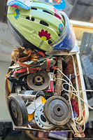 Photo showing a green bike helmet decorated with multicolored flowers on top of a box filled with various items including hand tools, cords, and miscellaneous parts.