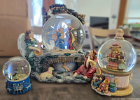 Photo showing three snow globes: a large nativity scene globe with angels, a mid-size Boyds Bears globe on an antiques base, and a small Disney castle globe.