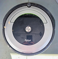 Top view of the iRobot Roomba vacuum showing the circular design, central Clean button, and visible dust/dirt on surface.