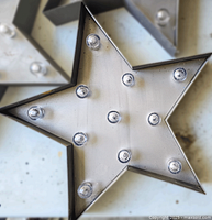Close-up photo of one star marquee sign showing metal frame, silver finish, multiple clear bulbs in sockets, surface rust and wear.