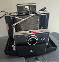 Front and opened view of the Polaroid Automatic 100 Land Camera displaying bellows, lens, and viewfinder.