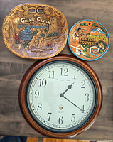 Clock and two collector plates on wooden surface showing the entire lot.