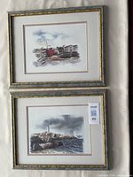 Photo of two framed art prints stacked vertically showing coastal scenes with boats and lighthouse