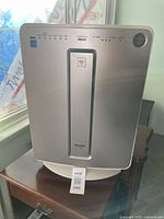Front view of the Sharp air purifier showing the full device on a wooden table near window.