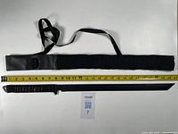 Full view of black katana blade with nylon sheath placed alongside a yellow measuring tape showing approximately 23 inches length