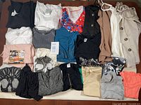 Photo displays various women's tops laid out on a surface, showcasing variety in colors and styles, mostly short sleeve and sleeveless tops.