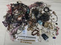 Overview of assorted jewelry laid out including necklaces, bracelets, earrings, pins, and rings in various styles and colors.