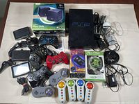 Photo showing entire lot with PlayStation 2 console, multiple controllers, Logitech speakers, Game Switch adapter box, Max Live controller in box, and various cables.