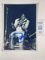 Black and white photo of James Brown singing on stage, hand-signed in blue ink, stored in a plastic sleeve.