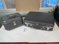 Photo showing both the vintage black suitcase and smaller travel case side by side on a white surface near a window.