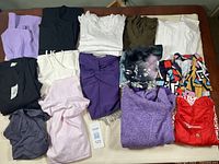 Photo of assortment of various medium-sized tops in multiple colors and patterns, folded and laid out on white surface