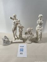 Five white Greek-style statues on a table with a Maxsold lot card.