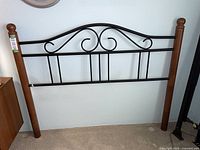 Full view of queen size headboard with solid wood posts and decorative metal center swirl design, standing against wall.