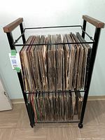 Full view of the black metal and wood record stand filled with two rows of vinyl records.