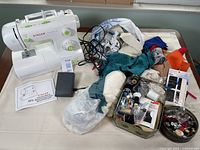 Singer Esteem II sewing machine with manual, foot pedal, and assorted fabrics and sewing supplies spread on table