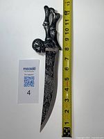 Full view of decorative cutter with skull handle beside measuring tape showing approx. 12 inch total length.