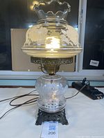Full lamp showing entire item with metal base, etched glass globe and light on, power cord visible.