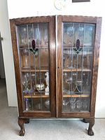 Full front view of the oak display cabinet showing double glass doors, shelves and carved legs