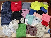 Photo showing an assortment of new women's XS tops, shorts, and pants in various colors and styles, including a white lace-up corset style top and a red crocheted short-sleeve top.