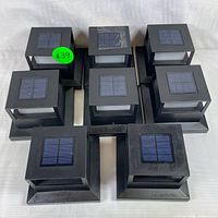 Eight black solar-powered fence lights arranged on a white surface, showing the top solar panels and overall design.