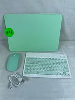 Photo showing mint green wireless keyboard, matching mouse, and white charging cable all laid out on a striped white surface