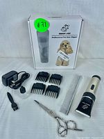 Pet hair clipper with attachments, scissors, comb, brush, oil, and power adapter shown next to original packaging box