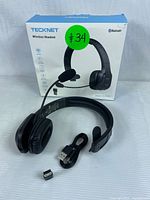 Front view of the Tecknet wireless headset with USB cable and Bluetooth adapter in front of the product box showing model TK-HS001 and branding.