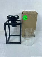 Front view of black metal rectangular tealight holder, clear glass shade, and boxed packaging.